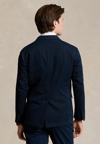 Blazer in cotone blu navy con design strutturato, spacco singolo sul retro e polsini con bottoni. Vestibilità sartoriale con texture liscia.