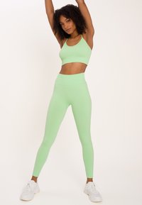Light green ribbed athletic set featuring a cropped tank top and high-waisted leggings, paired with white sneakers on a neutral background.
