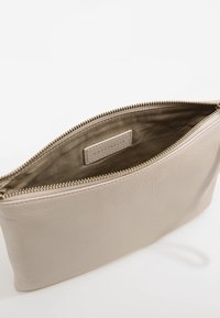 Bustina in pelle beige con esterno testurizzato, chiusura con cerniera e fodera interna liscia. Presenta una piccola etichetta del marchio all'interno.