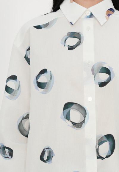 Camisa blanca de botón con patrones circulares abstractos en tonos de azul y verde. Tela ligera y semi-translúcida con un diseño de collar clásico.