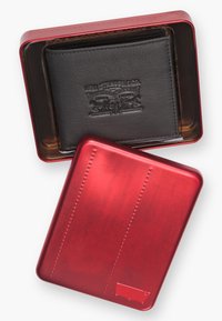 Svart läderplånbok med präglad logotyp inuti en glänsande röd metallburk, med en slät textur och subtila horisontella linjer på locket.