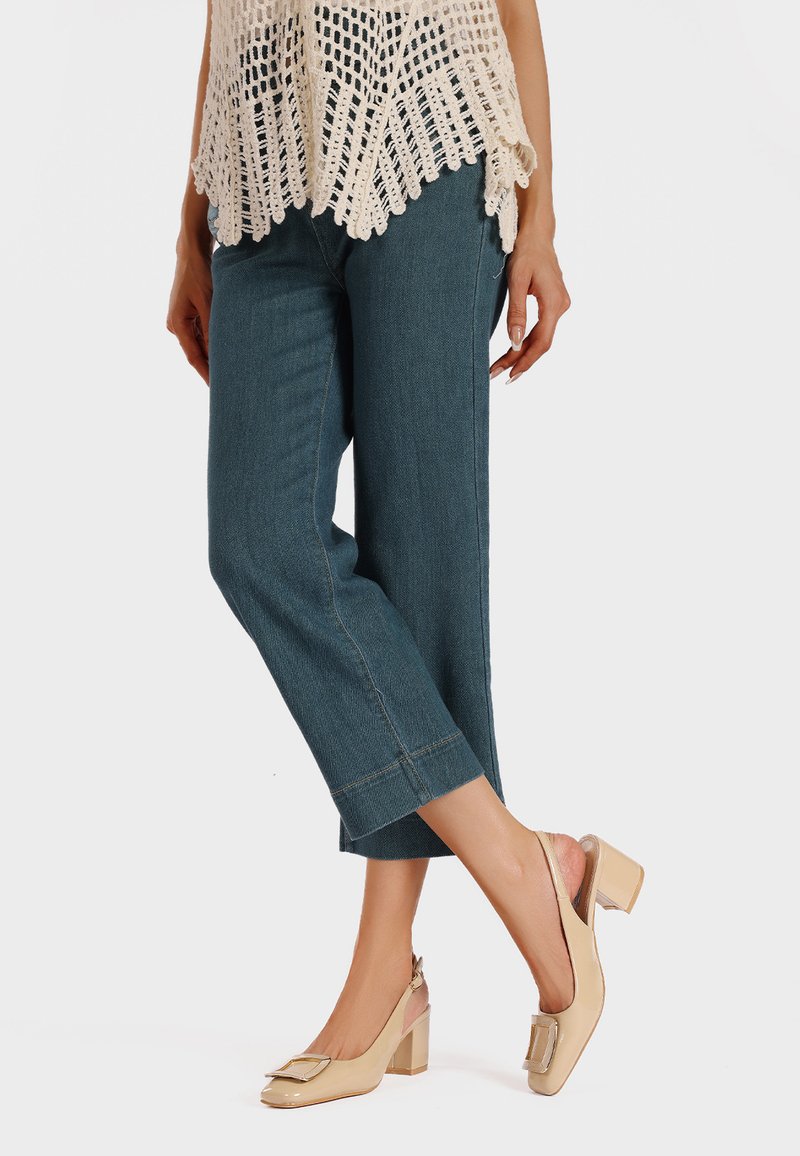 Maglione leggero a maglia aperta, jeans in denim blu a gamba dritta e décolleté nude con tacco a scomparsa, punta quadrata e dettaglio di fiocco decorativo.