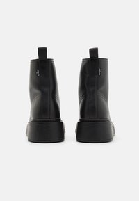 Mustad mustad ja elastsete külgpanelidega must nahast ankle saapad, millel on sile viimistlus ja paksud kummised tallad stabiilsuse tagamiseks. Omab minimaalset õmblusdetailide kujundust.