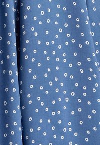 Tessuto blu con una sottile trama, caratterizzato da motivi circolari bianchi sparsi. Il design è giocoso e distribuito in modo uniforme su tutto il materiale.