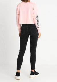 Camisa rosa corta de manga larga con letras negras en la manga, combinada con jeans negros ajustados de cintura alta y zapatillas negras con suela blanca.