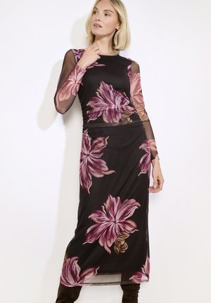 Largo vestido negro con mangas largas transparentes, que presenta grandes patrones florales en rosa y púrpura, con una silueta ajustada y una textura suave.