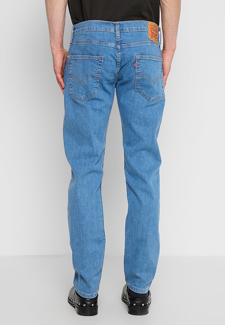 Jean en denim bleu clair avec une coupe droite, comportant des coutures visibles, deux poches arrière et une étiquette de marque en cuir sur la taille.