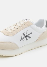 Sneaker Calvin Klein Jeans in bianco e beige. Presenta una parte superiore in synthetic liscia con dettagli in suede, lacci piatti e suola rialzata.