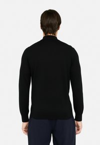 Maglione nero a maniche lunghe con una texture liscia, scollatura rotonda e polsini aderenti, abbinato a pantaloni scuri.