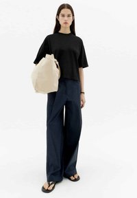 Schwarzes T-Shirt mit kurzen Ärmeln und lässiger Passform, kombiniert mit dunkelblauen weit geschnittenen Hosen und einer beigen Tasche mit gerundetem oberen Teil und Schulterriemen.