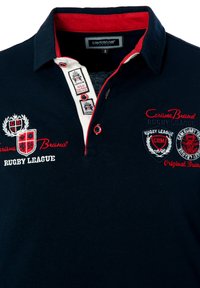Tumesinane polo särk punaste kaeluse aktsentidega, millel on broderitud logod ja tekst. Valmistatud puuvillast, kontrastsete nuppudega.