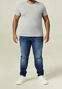 Harmaa lyhythihainen t-paita yhdistettynä sinisiin farkkuihin. Farkuissa on kulunut ilme, ja ne on viimeistelty valkoisilla lenkkareilla.