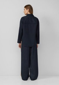 Navy gestreiftes Hemd und weit geschnittene Hose, mit einem Button-Down-Kragen und subtiler Textur. Vertikale Streifen sorgen für visuelles Interesse.