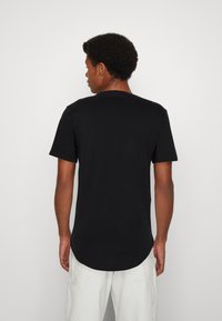 Schwarzes T-Shirt mit kurzen Ärmeln, abgerundetem Saum und Rundhalsausschnitt, das über eine glatte Textur und ein einfaches, minimalistisches Design verfügt.