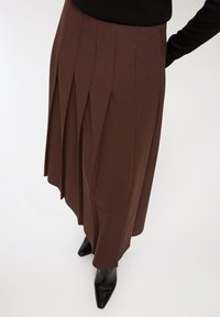 Gonna midi plissettata marrone realizzata in tessuto morbido con vita alta e chiusura con zip, abbinata a décolleté nere a punta.
