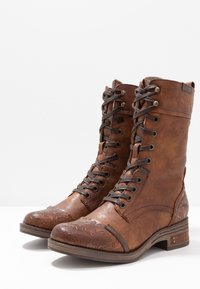 Brązowe skórzane botki na sznurówki z teksturowanym wykończeniem na czubku, dekoracyjnymi akcentami i średniej wysokości krojem. Płaski, warstwowy obcas.