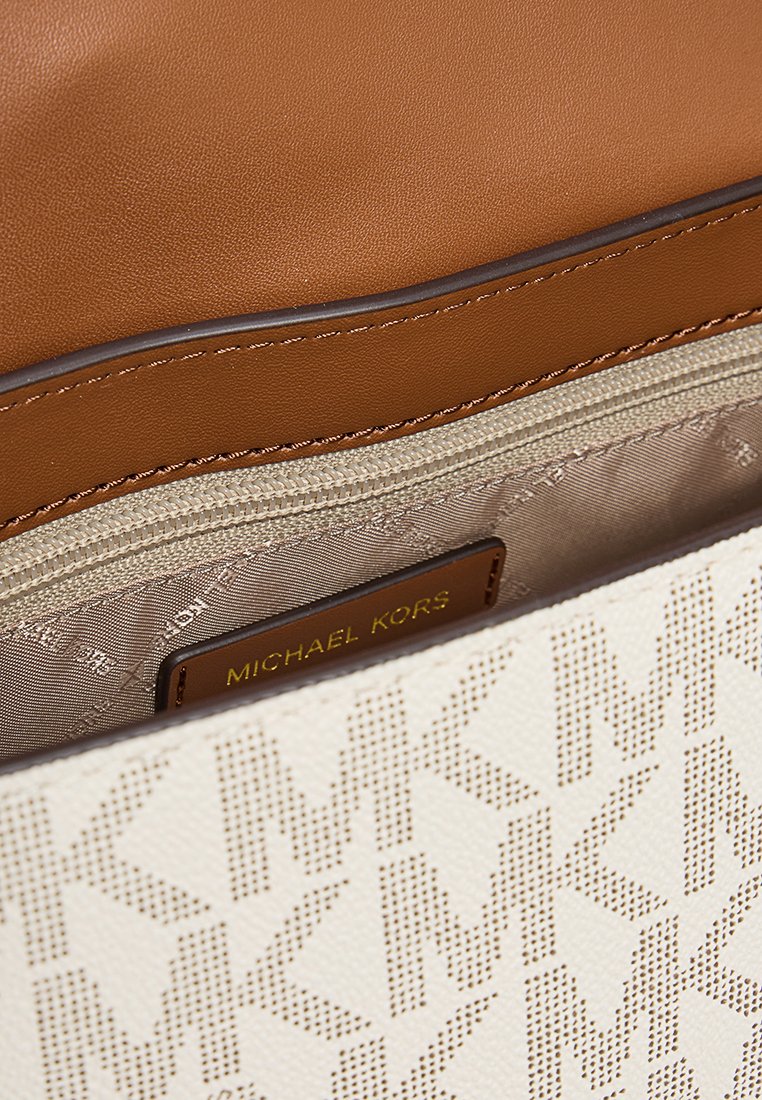Sac à main Michael Kors avec un extérieur à motifs blancs, des bordures en cuir beige, et un intérieur beige avec une poche zippée.