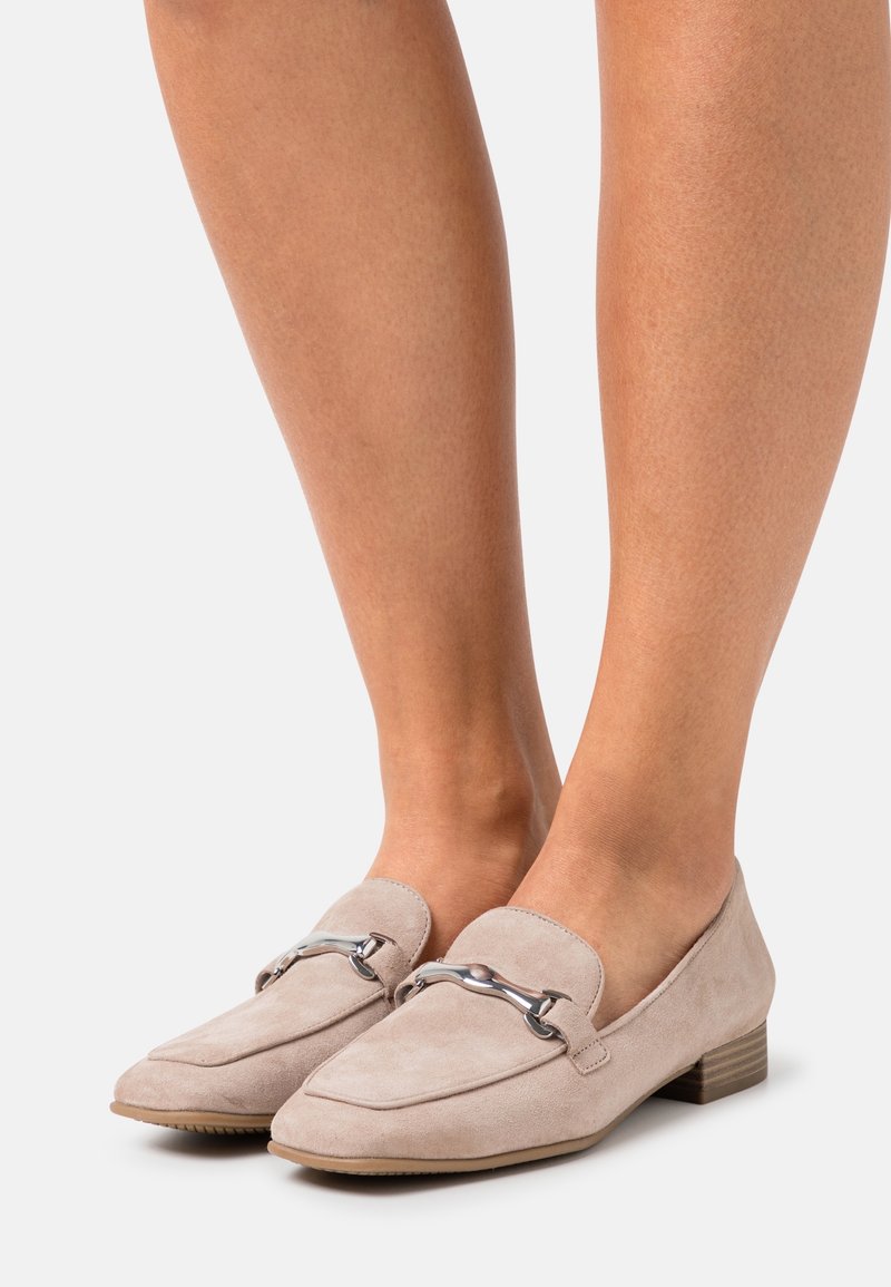 Mocassins plats en daim beige avec un détail en métal argenté sur le dessus, portés aux pieds, dotés d'un petit talon empilé et d'un bout carré arrondi.