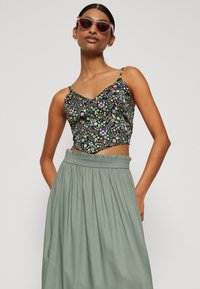 Top preto cropped com um padrão floral colorido, combinado com uma saia plissada de altura alta em verde claro. Inclui alças finas e cintura elástica.