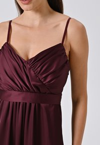 Mauve mouwloze jurk met geplooide bovenkant, v-hals en een nauwsluitende tailleband. Gemaakt van een soepele, lichte stof.