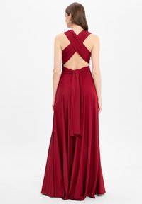 Langes, burgunderfarbenes Abendkleid mit tiefem V-Rücken und überkreuzten Trägern. Aus weichem Stoff gefertigt, zeichnet es sich durch eine fließende Silhouette und eine gebundene Taille aus.