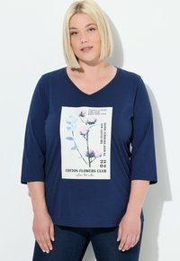 T-shirt blu navy a scollo a V realizzato in tessuto morbido, con una grafica stampata floreale e testo su sfondo bianco, maniche a 3/4, vestibilità comoda.
