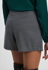 Shorts a vita alta in un motivo pied-de-poule bianco e nero, con una texture liscia e una vestibilità sartoriale, caratterizzati da un design posteriore semplice.