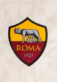 Logo con bordes negros en forma de escudo que presenta un lobo gris y dos bebés, coloreado en amarillo y marrón. Texto: "ROMA" y "1927" en la parte inferior.