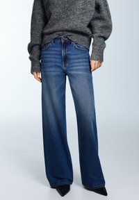 Széles szárú, kék farmernadrág magas derékkal, enyhén kifakult hatással, klasszikus öt zsebes kialakítással és diszkrét varrási részletekkel.