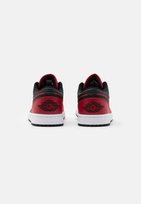 Röda och svarta sneakers med en slät läderfinish, vita gummisulor och präglade logodetaljer på baksidan.
