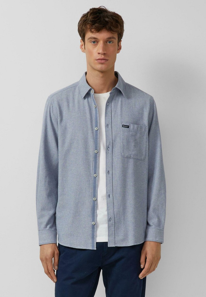 Camicia azzurro chiaro con bottoni, dotata di tasca, realizzata in un tessuto testurizzato. Design semplice con orlo arrotondato e colletto standard.