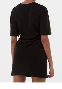 Musta lyhythihainen t-paita mekko, ylipitkä muotoilu, sileä pinta, laskeutuu reiden keskikohtaan, pyöreä pääntie, minimaalinen ompeluyksityiskohta.