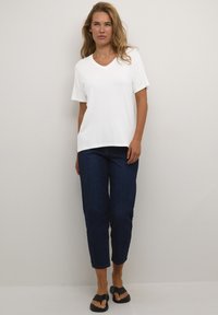 T-shirt en coton blanc à col en V associé à un jeans en denim bleu foncé. Le mannequin porte des sandales à glissière noires. Design simple et décontracté.