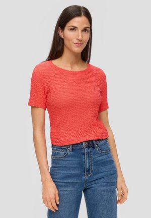Haut court à manches courtes texturé corail avec un col rond, accompagné d'un jean bleu taille haute. Le haut présente un design de tissu légèrement froissé.