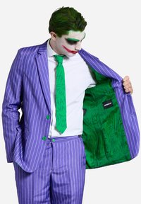Completo a righe viola con bottoni e cravatta verdi. Camicia bianca, fodera interna verde con motivo "HA". L'attore dimostra l'interno della giacca.