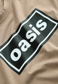 Beige Baumwoll-T-Shirt mit einem großen schwarzen rechteckigen Druck, auf dem das Wort "oasis" in Weiß steht. Es zeichnet sich durch eine glatte Textur und ein lässiges Design aus.