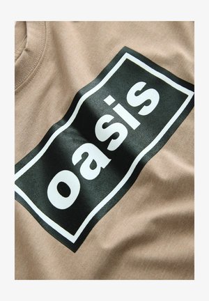 Beige pamut póló, amelyen egy nagy fekete téglalap alakú nyomat található, rajta a "oasis" szó fehér színben, sima textúrával és laza dizájnnal.
