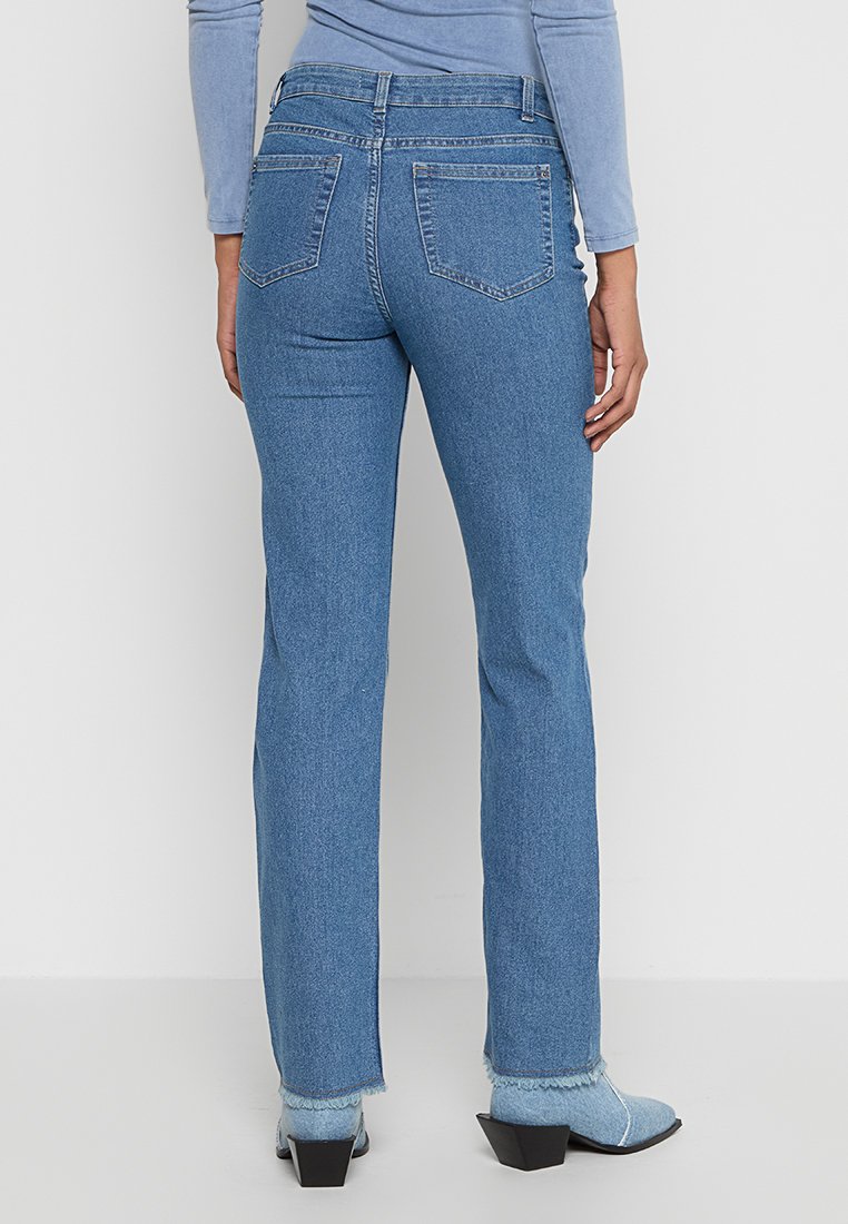 Lichtblauwe denim jeans met een rechte pijpdesign, voorzien van achterzakken en een rafelige zoom, gecombineerd met zwarte hoge hakken.