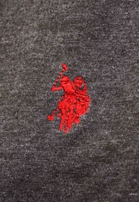 Rotes gesticktes Logo eines Polo-Spielers zu Pferd, der einen erhobenen Schläger auf dunkelgrauem Strickstoff hält.