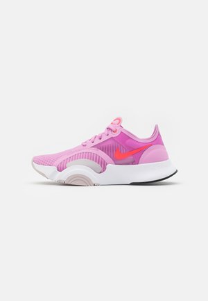 Chaussure de running Nike rose et violette avec un swoosh rouge, semelle blanche et beige clair, affichée sur un fond blanc uni.