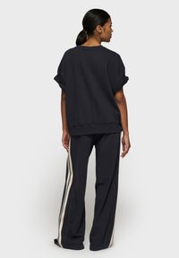 Marineblå oversized sweatshirt med oprevne ærmer, sammen med løstsiddende marineblå bukser med cremede lodrette striber på siderne.