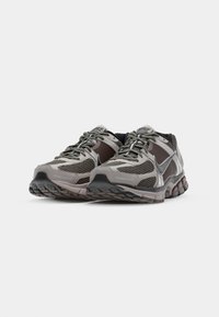 Nike tornacipők szürke és fekete árnyalatokban, hálós panelek, texturált talpak és fűzők jellemzik őket. Megerősített orr-részek és látható márkajelzések.