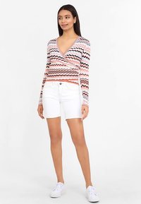 Long-sleeve wrap sweater with a zigzag pattern in pink, orange, and black, paired with white shorts and white sneakers.