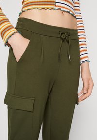 Olivgröna joggers med dragsko i midjan, sidofickor och fickor på benet. Tillverkade av mjukt, strukturerat tyg.