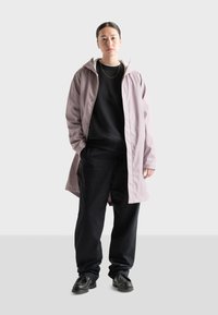 Svetloružová nepremokavá bunda s kapucňou, nosená cez čierny sveter, v kombinácii s čiernymi nohavicami a čiernymi topánkami. Jednoduchý dizajn so zúbkami.