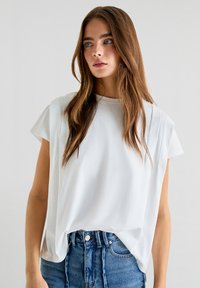 Hvid kortærmet top lavet af blød stof, med en afslappet pasform og rund halsudskæring, parret med højtrækkende blå denim jeans.