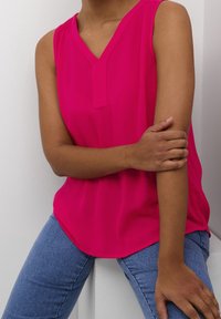 Fuksjowa bluzka bez rękawów z dekoltem w serek i subtelną teksturą, zestawiona z niebieskimi dżinsami. Prosty, casualowy design, z wyraźnymi liniami.