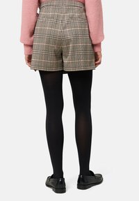 Beige ternede shorts med høj talje og baglommer, parret med sorte strømpebukser og sorte loafers. Sweateren er lyserød med ballonærmer.