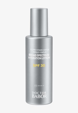 Bouteille cylindrique argentée de lotion hydratante à large spectre avec SPF 30, présentant un texte blanc et jaune détaillant les ingrédients et le nom de la marque.