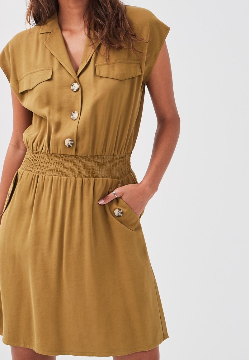 Robe à manches courtes de couleur moutarde, avec un devant à boutons, deux poches poitrine et une taille élastique, fabriquée dans un matériau doux et fluide.